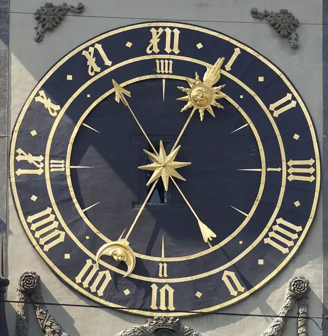 The eastern clock face of the Zytglogge tower in Bern, with gold Roman numerals on a dark dial; four o'clock is written IIII.